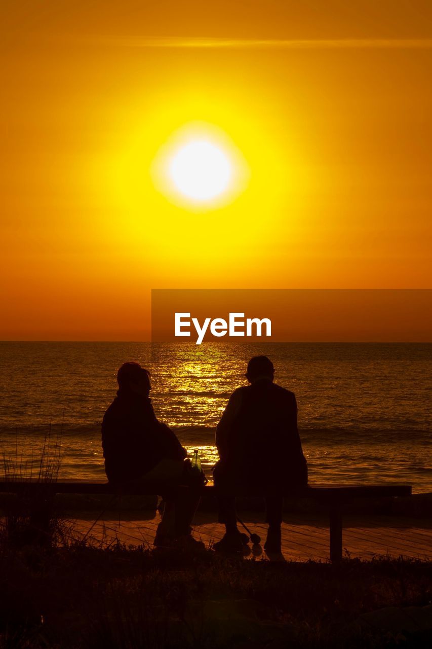 Silhouette man and woman sitting at beach during sunset