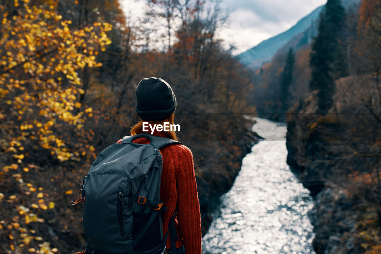 REAR VIEW OF MAN STANDING IN FOREST DURING AUTUMN