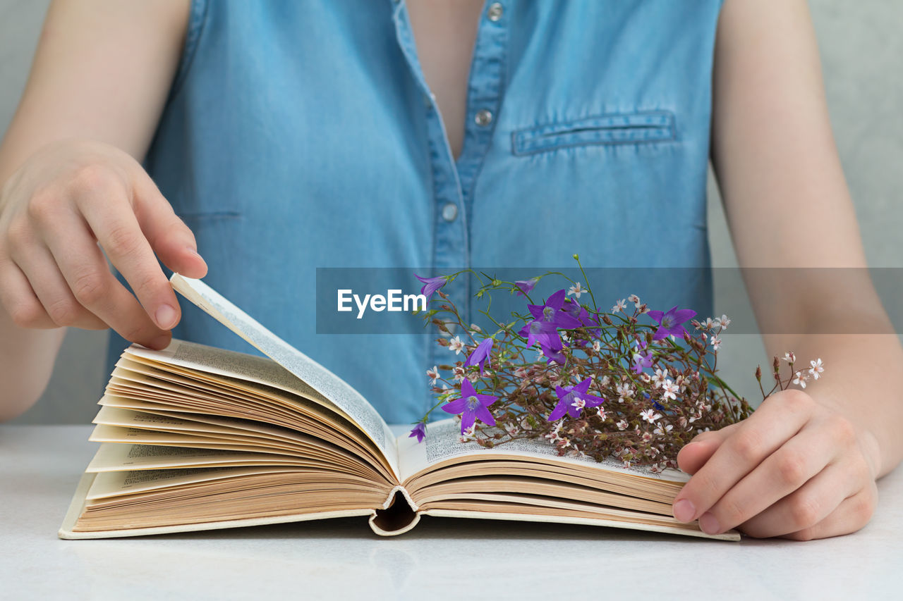 Midsection of woman reading book with flowers