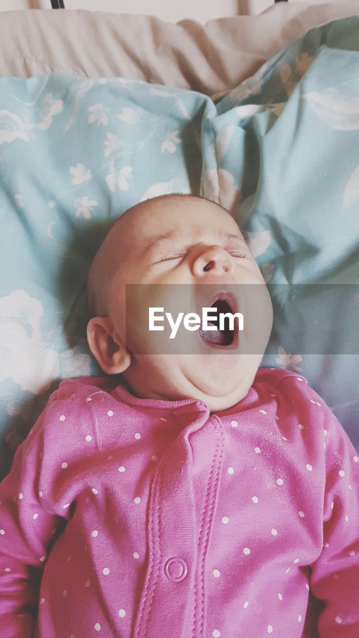 High angle view of cute baby yawning on bed at home
