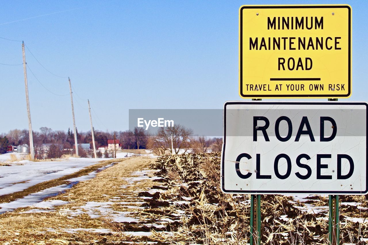 ROAD SIGN ON SNOWY FIELD AGAINST SKY