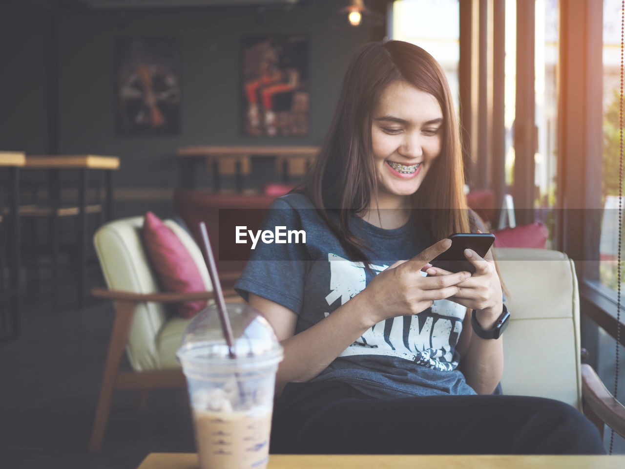 Smiling woman using mobile phone while sitting by drink on table