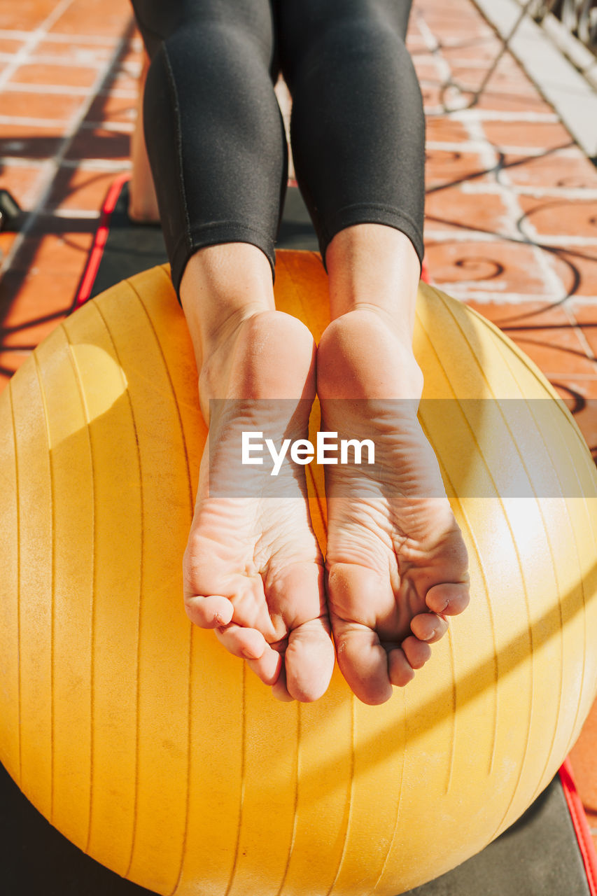 Female fitness instructor using yoga exercise ball outdoors in morning sunshine