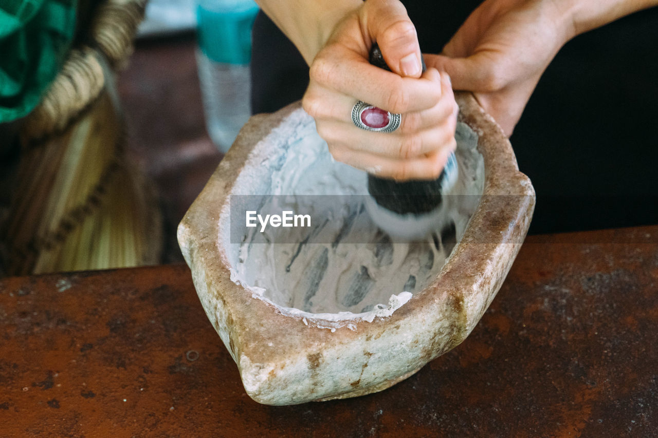 Close-up of woman mortar and pestle while preparing food at table