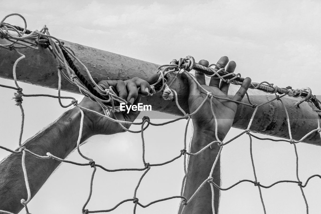 Cropped image of man attaching net on goal post against sky