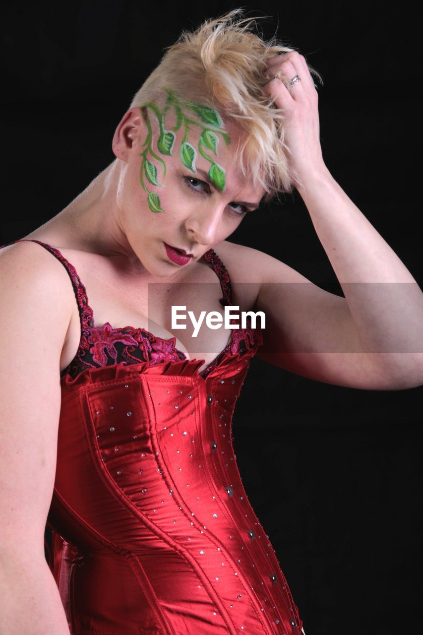 Portrait of young woman with face paint standing against black background