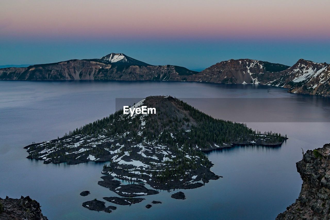 Scenic view of lake by snowcapped mountains against sky during sunset