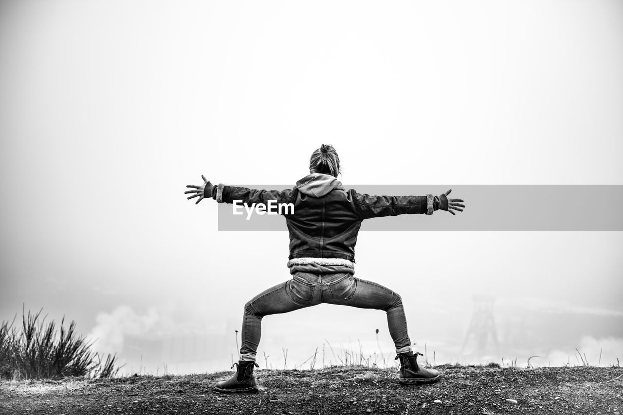 Woman with arms outstretched and legs apart standing on mountain during foggy weather