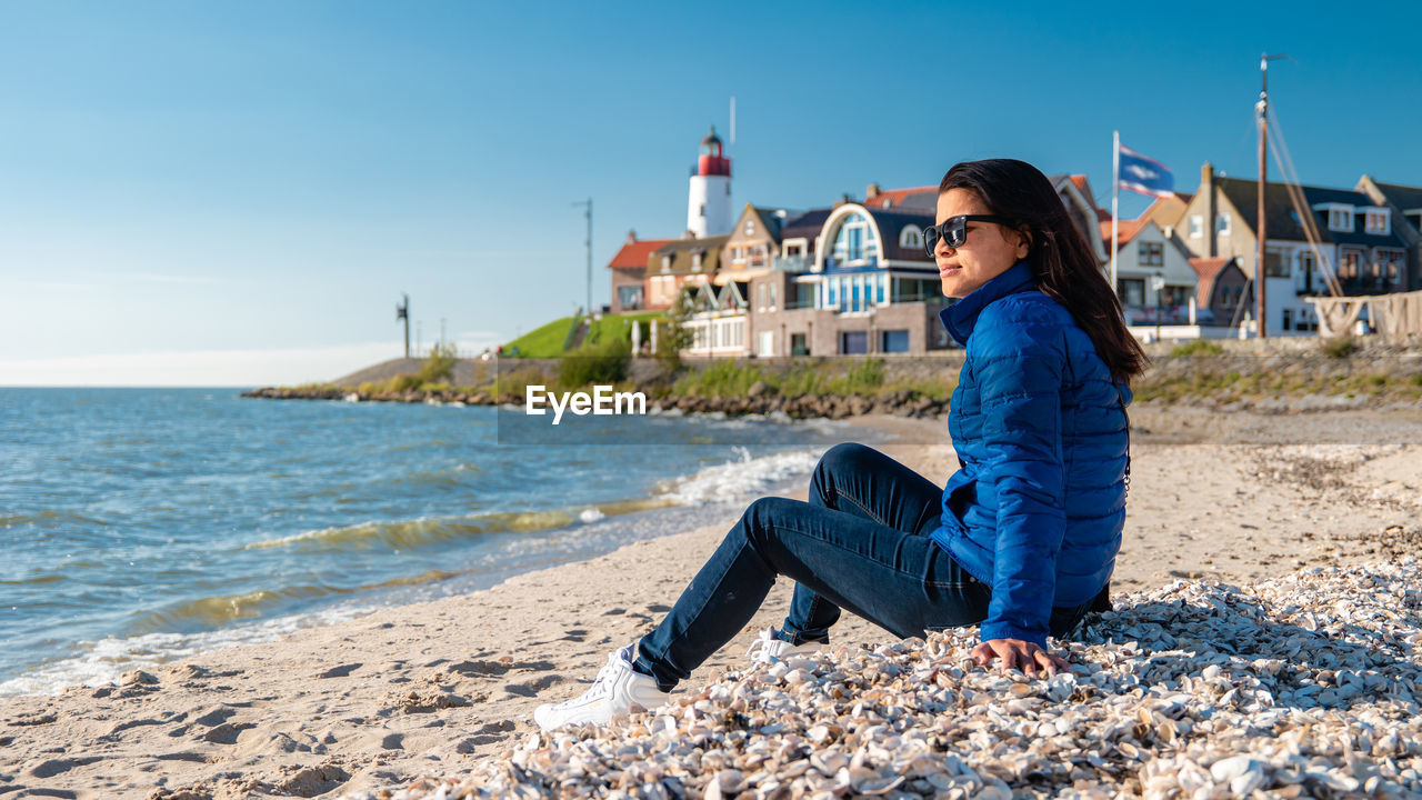 portrait of young woman sitting on beach against sky