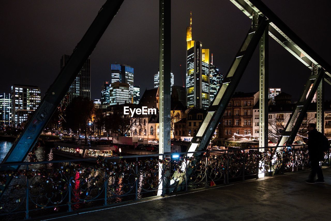 Illuminated bridge by buildings against sky at night