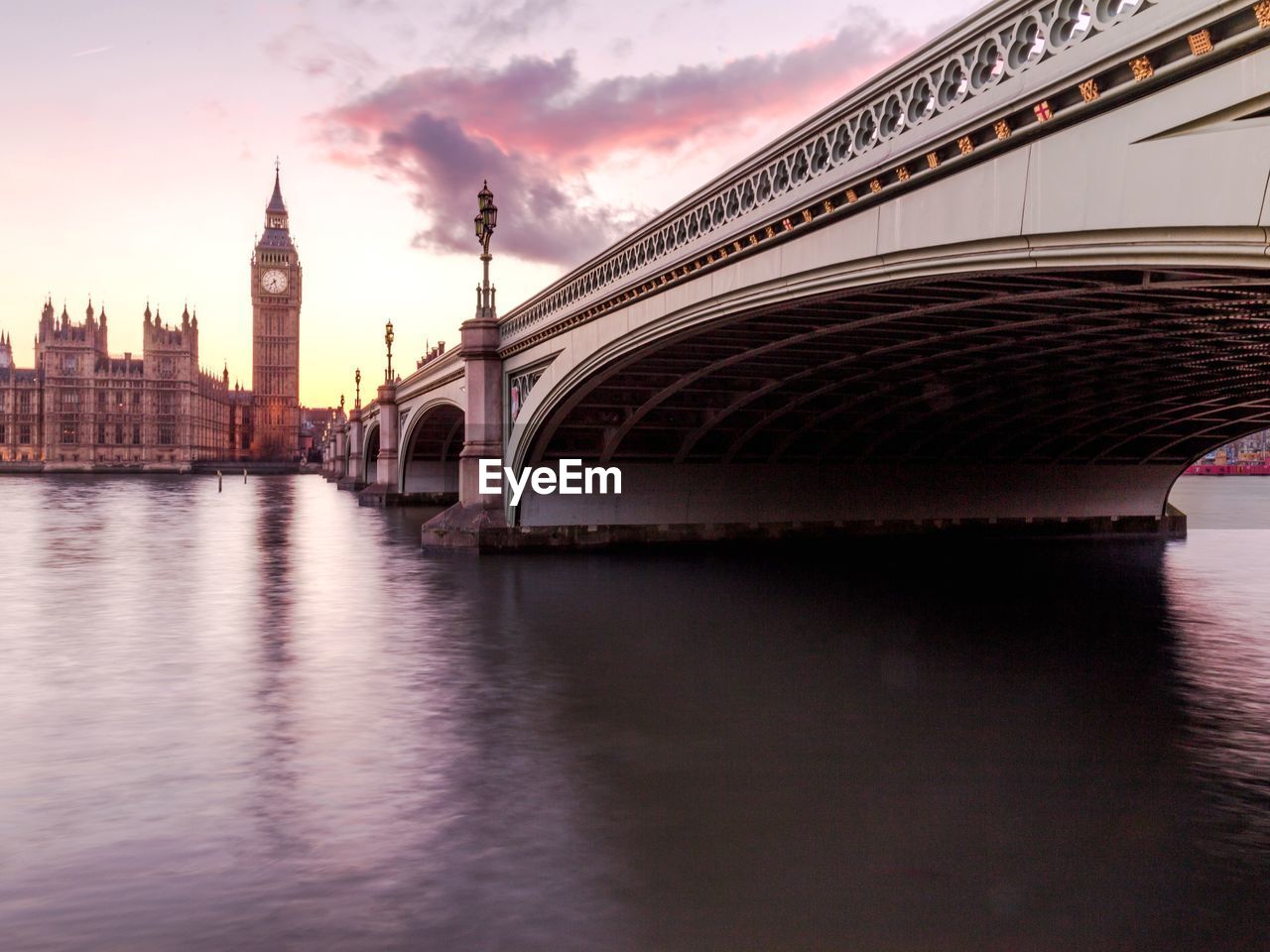 Westminster bridge by big ben over thames river against sky in city