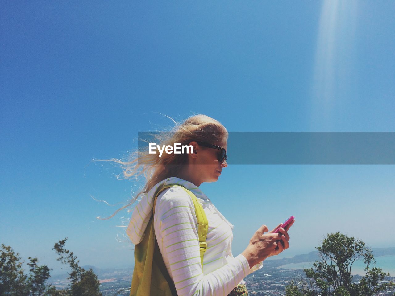 Side view of woman using mobile phone against blue sky