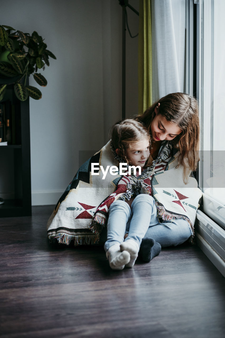 Girl sitting on sitter lap while sitting by window at home