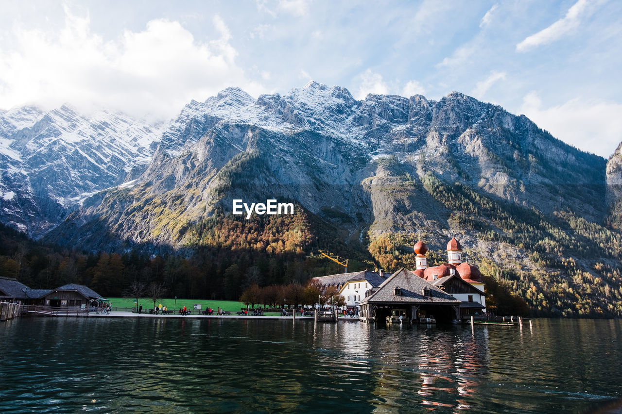 People on lake by mountain against sky