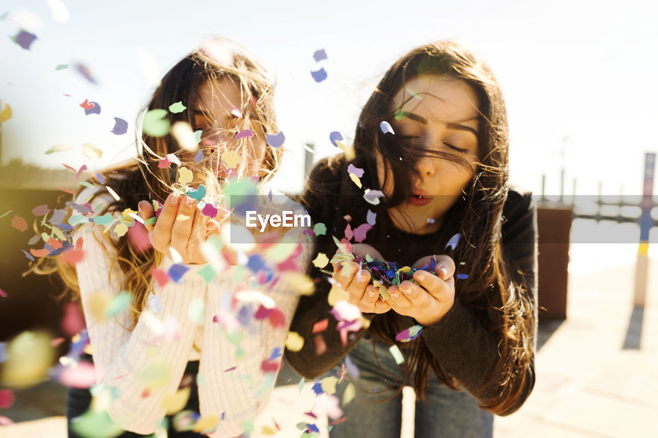 Young women blowing confetti during sunny day