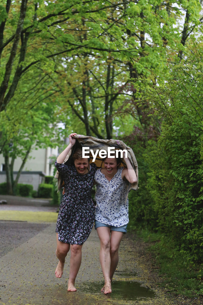 Two girls run barefoot under a raincoat and laugh.