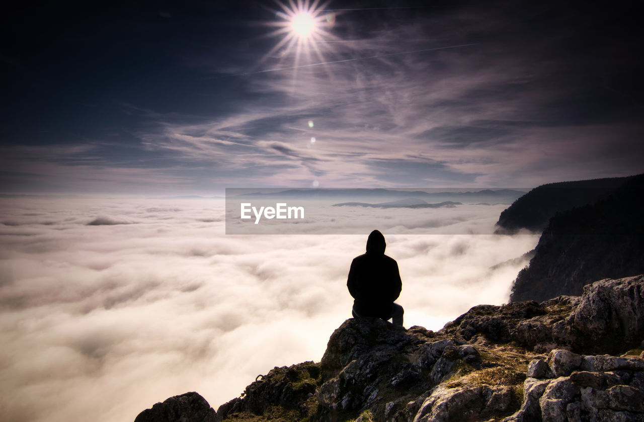 Rear view of silhouette man sitting on mountain against sky