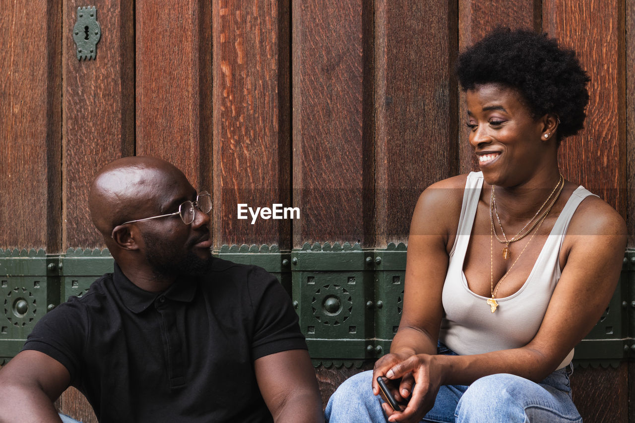 Amazed young african american female reacting on news from boyfriend while sitting together against wooden wall