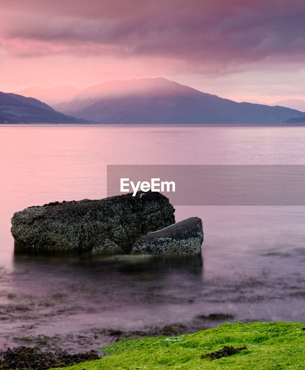 Scenic view of lake and mountains against cloudy sky during sunset