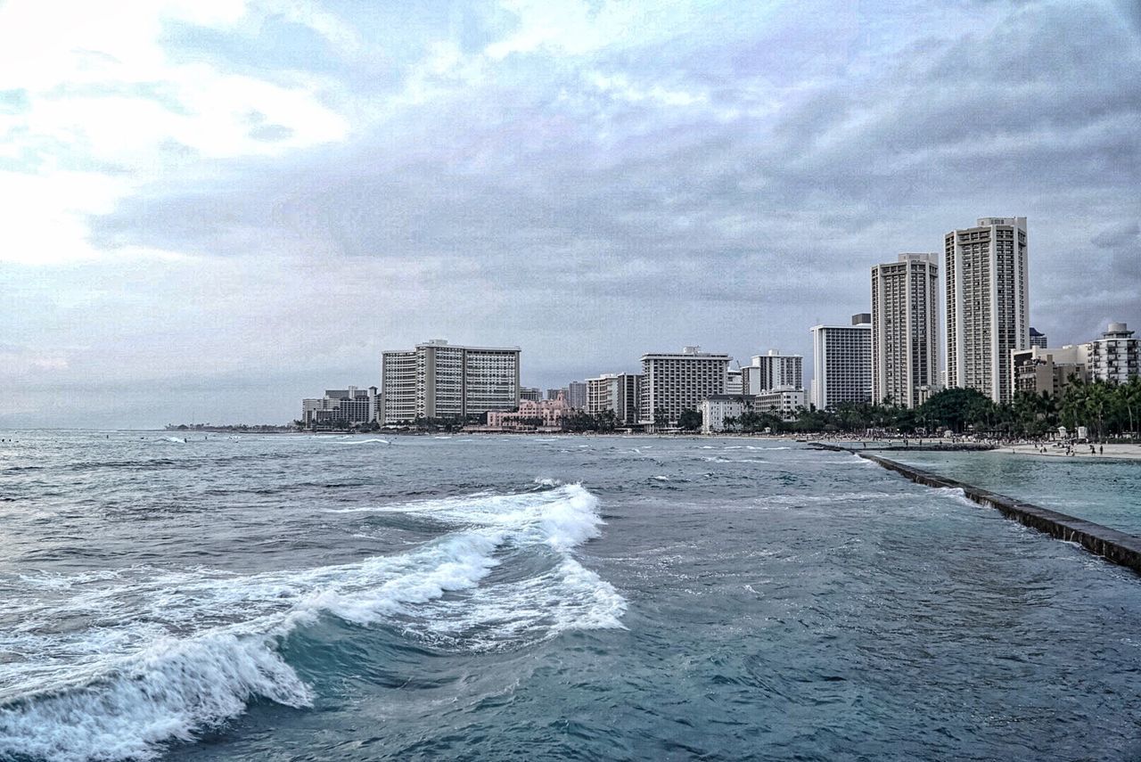 City skyline at sea against cloudy sky