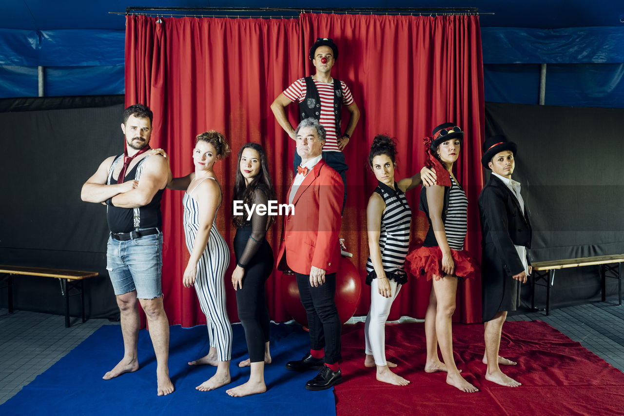 Confident circus performers standing together in front of red curtain on stage