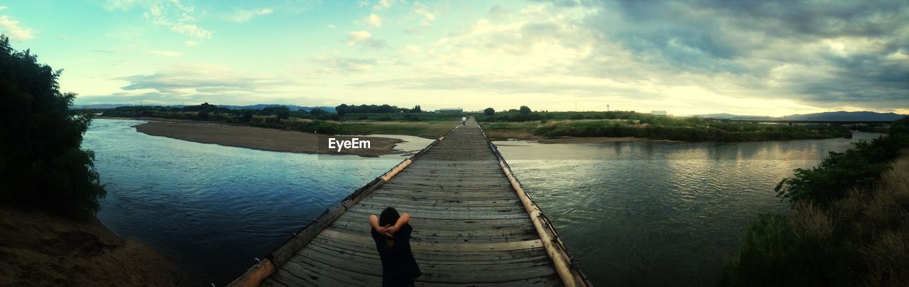 Rear view of person standing on jetty against lake