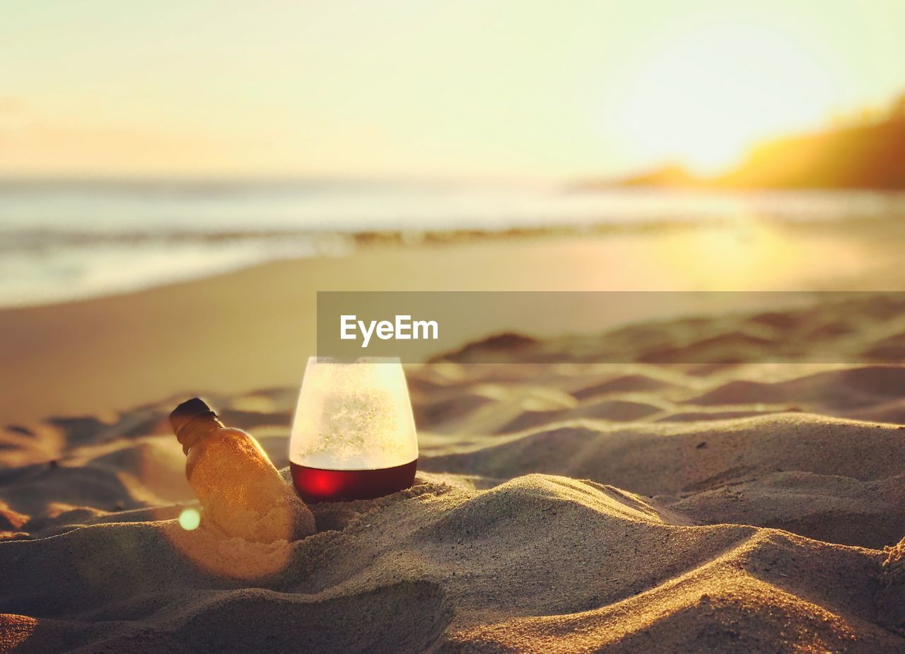 Coffee in glass on sand at beach against sky during sunset