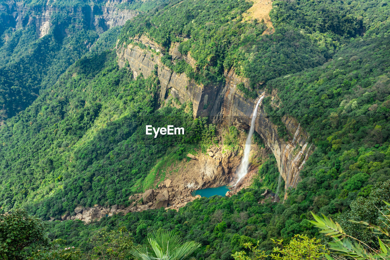 Waterfall streams falling from mountain top covered with green forests at day