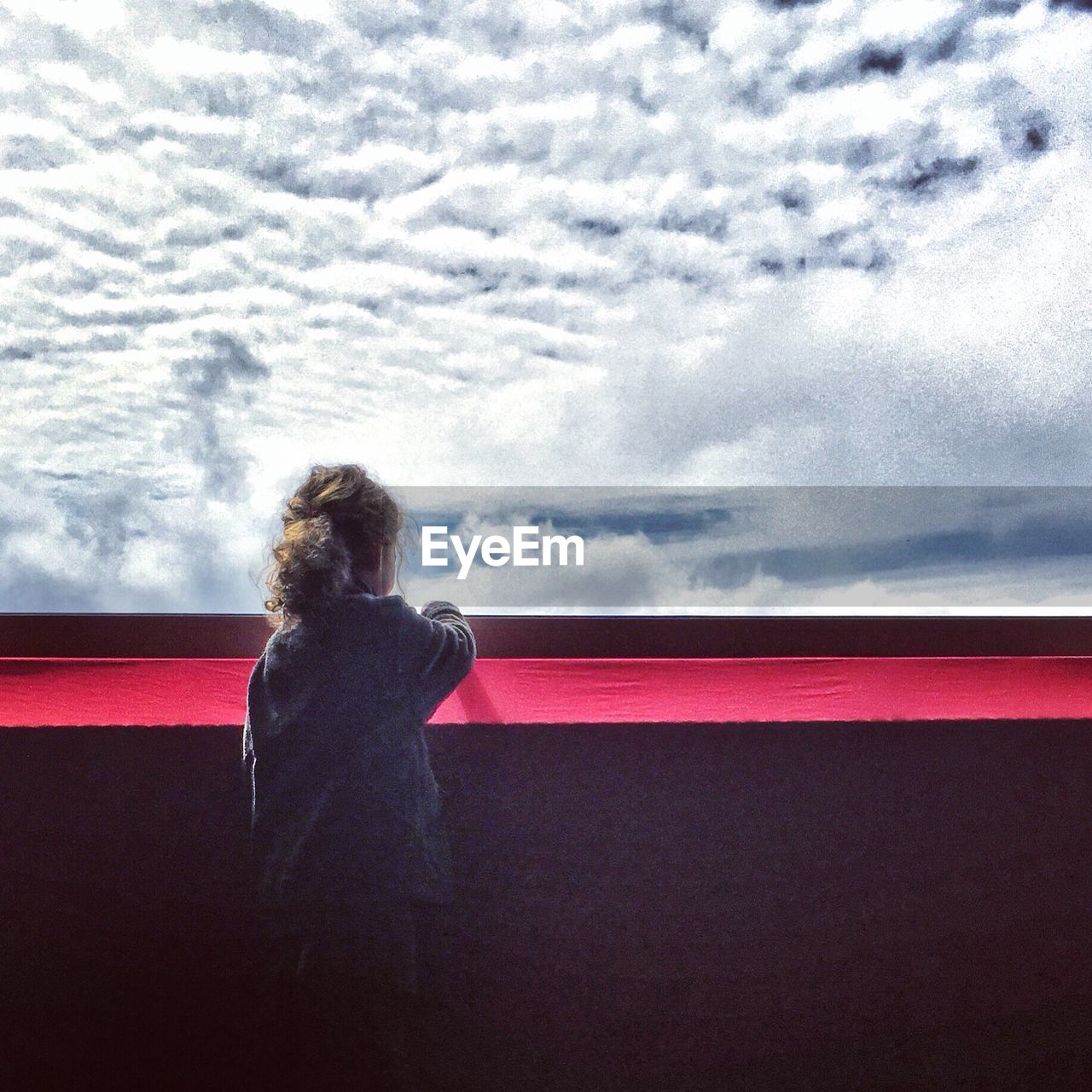 Rear view of girl on standing in balcony against cloudy sky