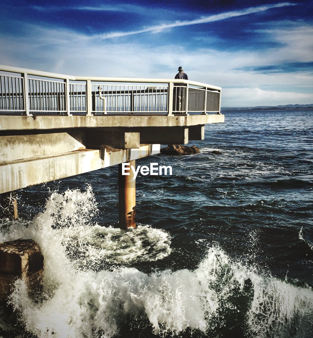 Man standing on pier at sea against cloudy sky