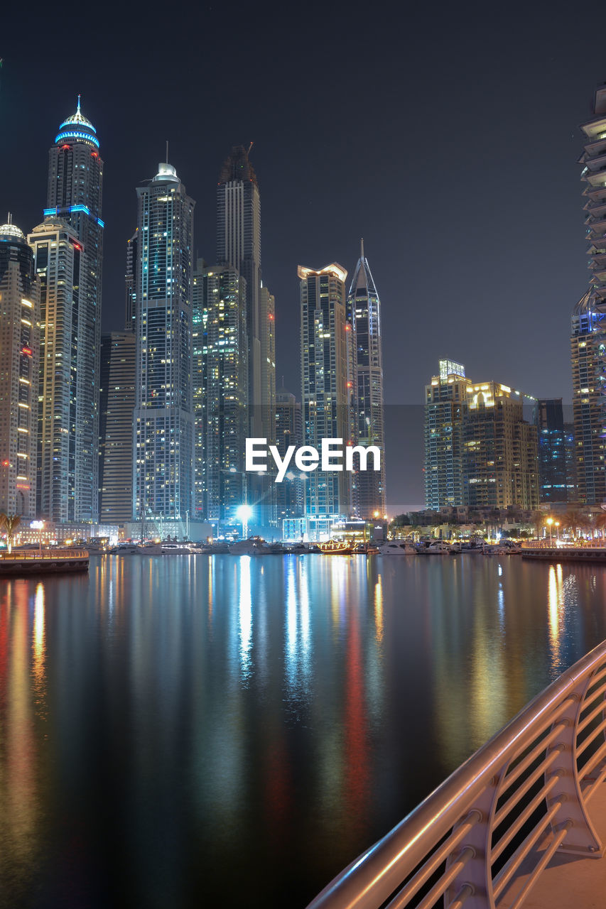 Illuminated buildings by river against sky at night