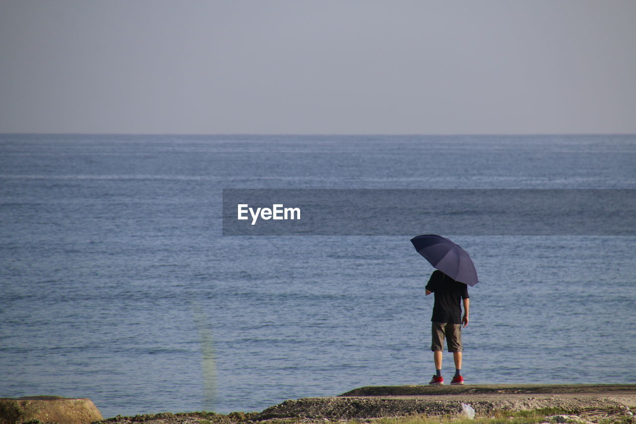 Rear view of woman standing by sea against clear sky