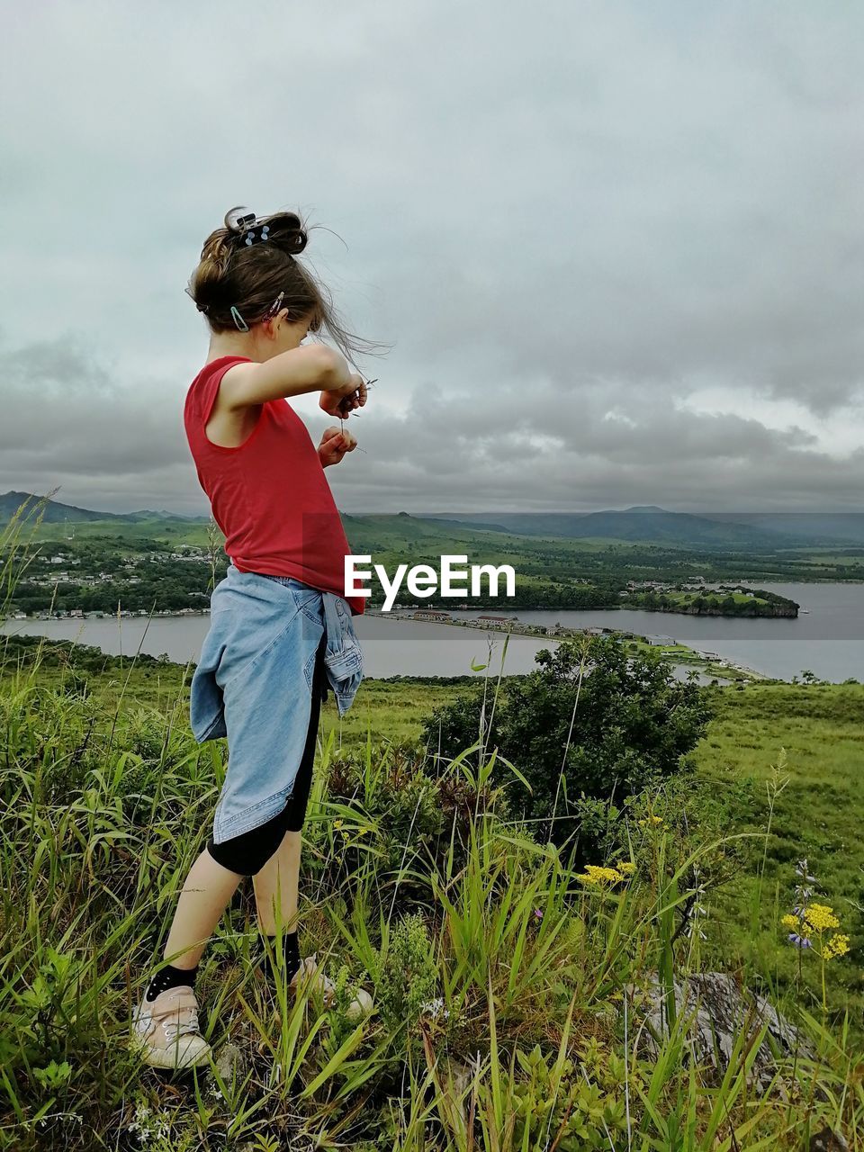 Girl in red t-shirt standing in the meadow against cloudy sky on a summer day