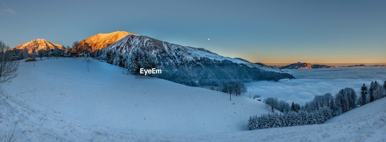 Snow covered land and mountains against sky during sunset
