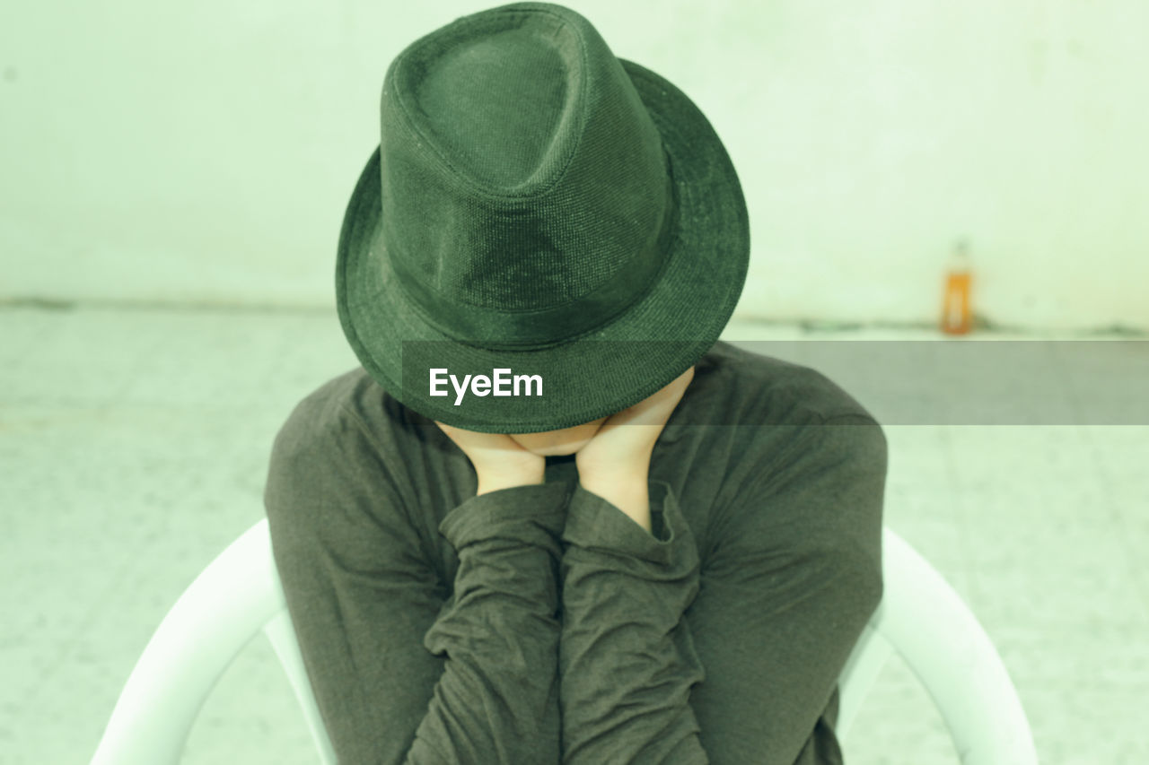 Close-up of woman wearing hat while sitting on chair against wall