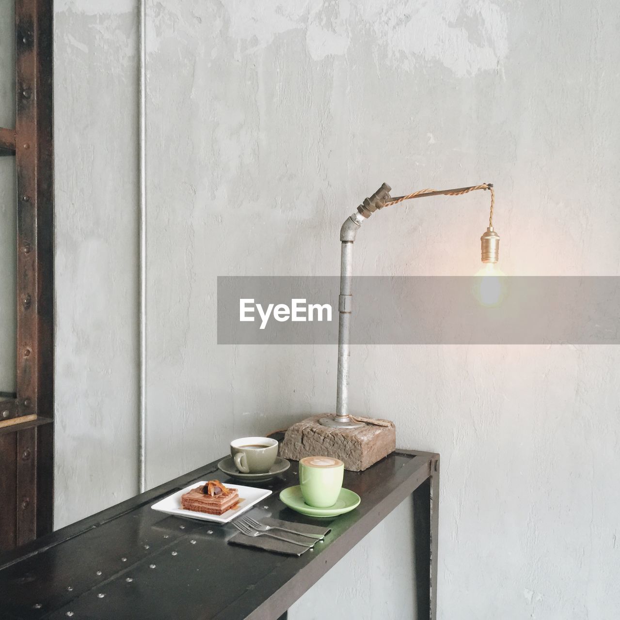 Breakfast on table by illuminated light bulb against wall