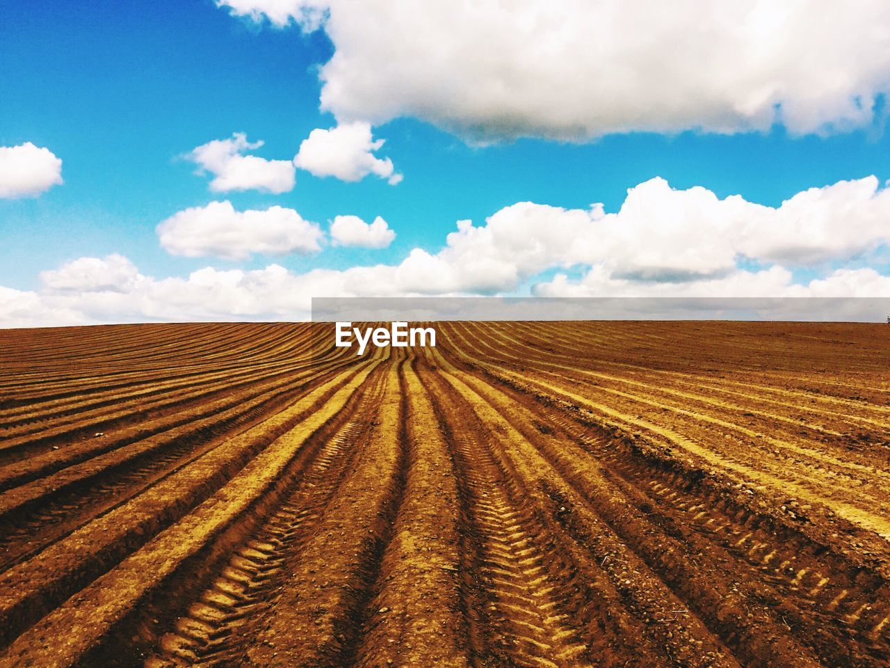 View of tire track in dirt field against cloudy sky