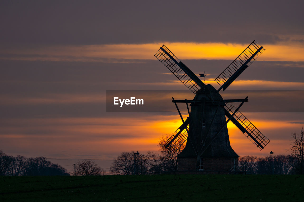 SILHOUETTE TRADITIONAL WINDMILL ON FIELD AGAINST SKY AT SUNSET