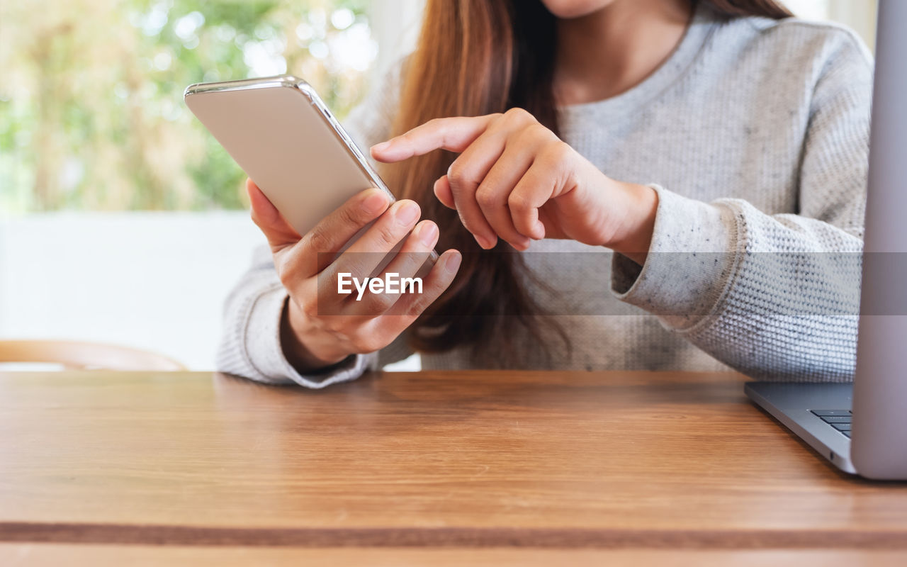 midsection of woman using mobile phone while sitting at table