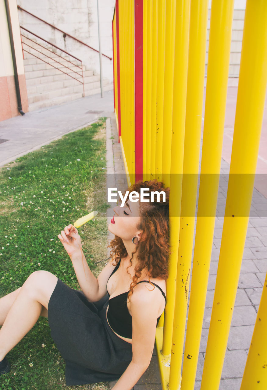 High angle view of woman having popsicle while sitting by yellow railing