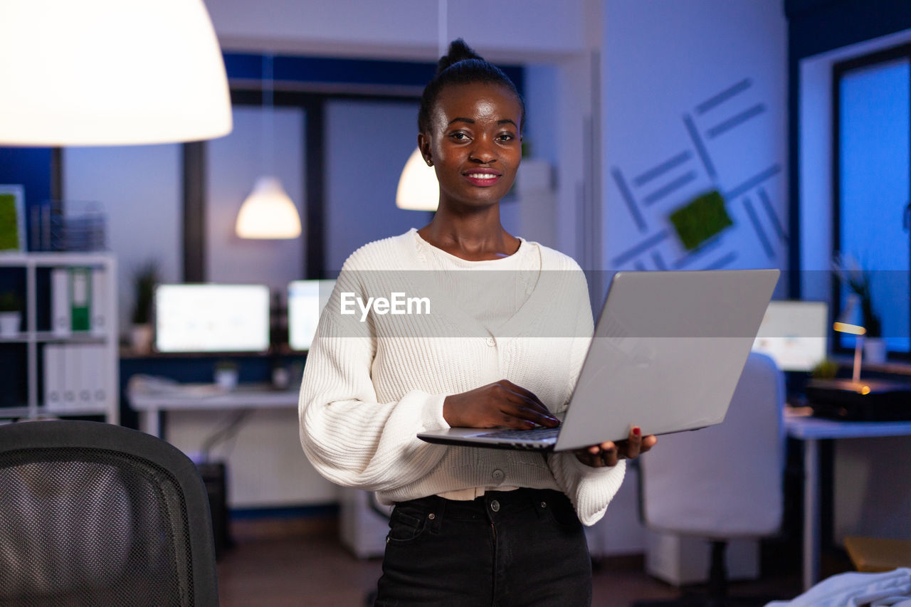 PORTRAIT OF SMILING YOUNG MAN USING LAPTOP IN OFFICE