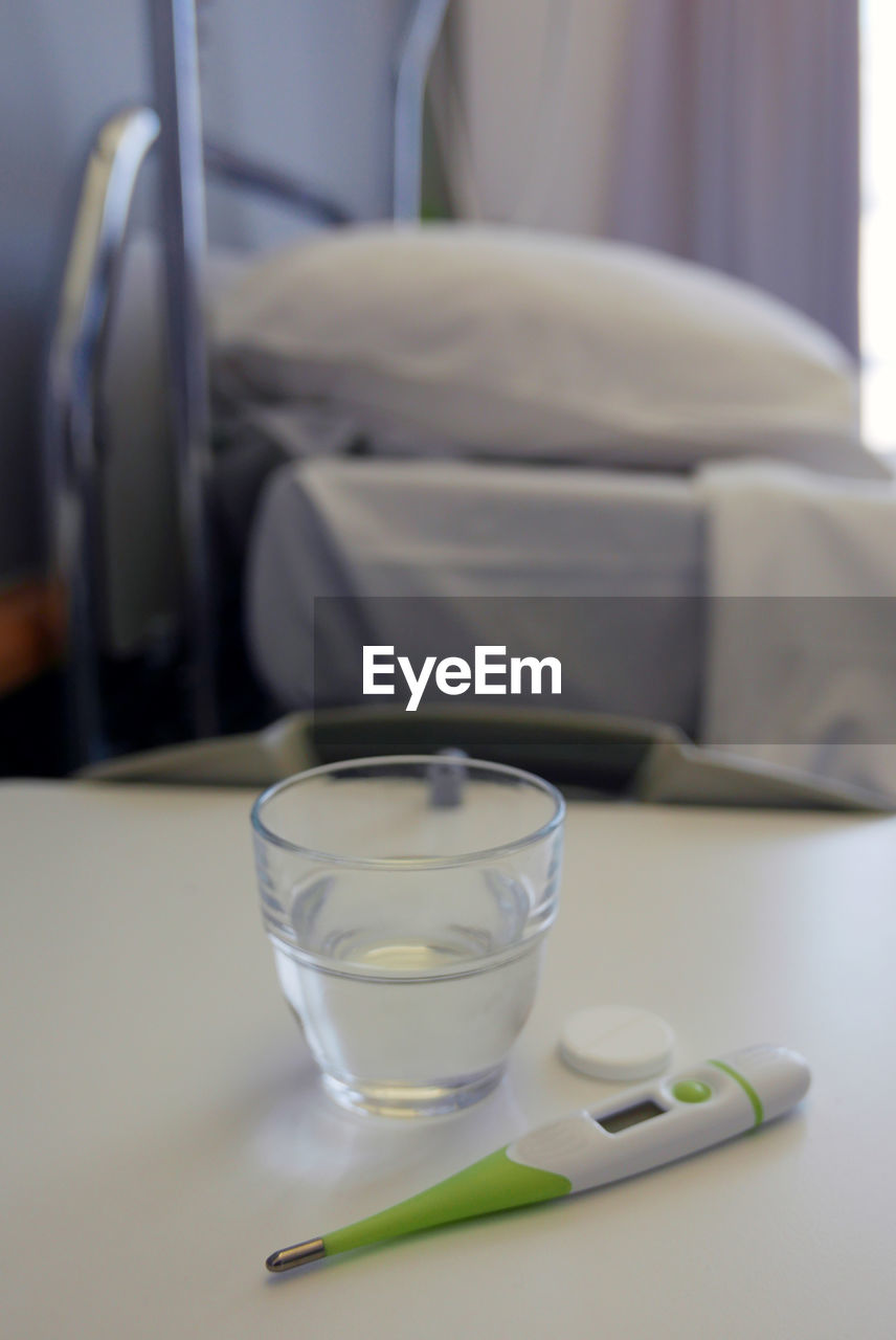 Pill and water glass with thermometer on table in hospital