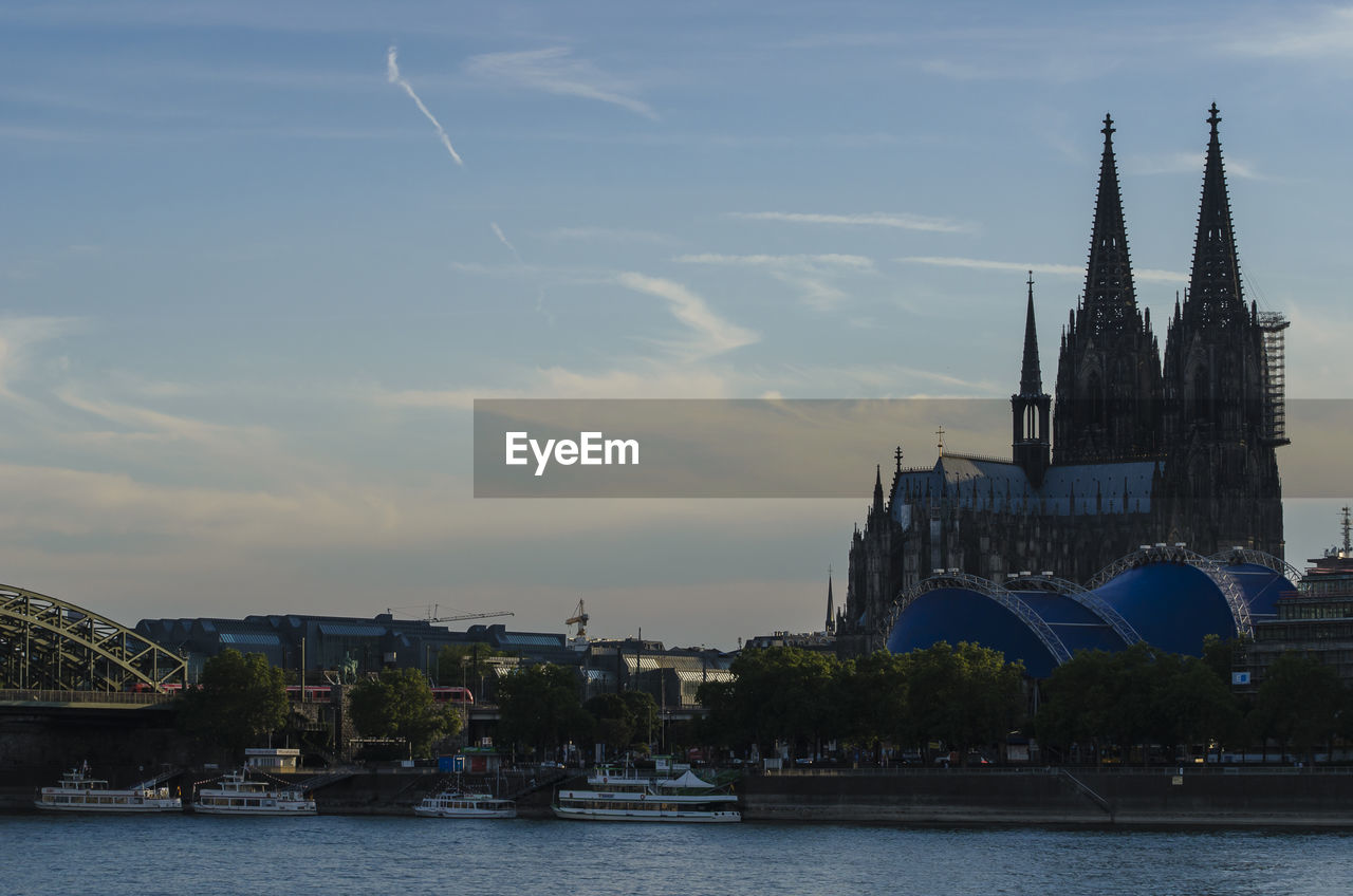 Cologne cathedral in city by river against sky during sunset