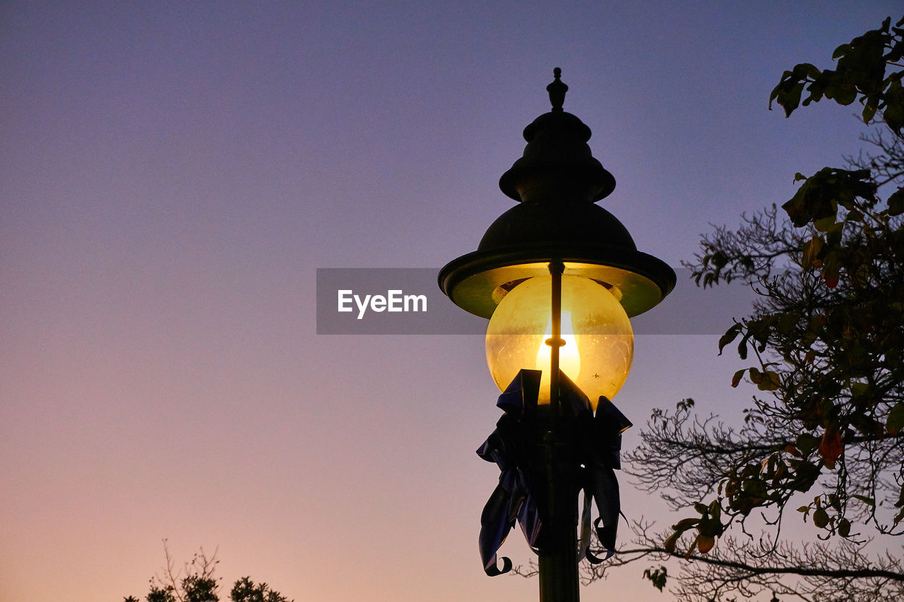 LOW ANGLE VIEW OF ILLUMINATED STREET LIGHT AGAINST SKY AT DUSK