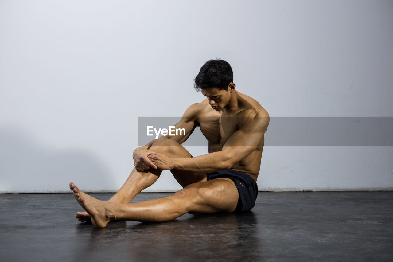 Shirtless muscular man sitting against wall