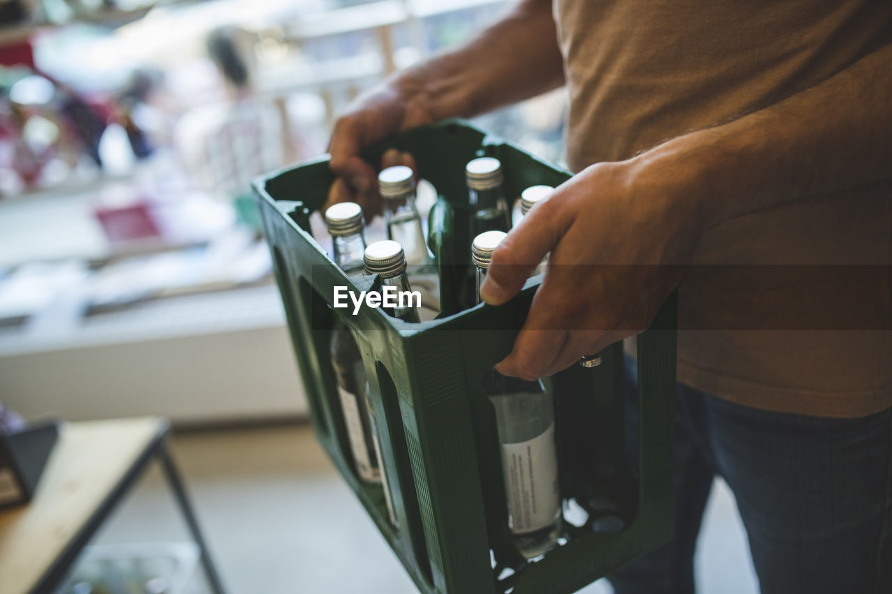 Midsection of salesman carrying bottles in crate at deli