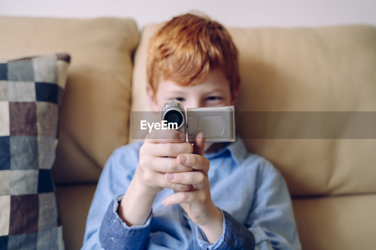 Portrait of boy holding camera while sitting on sofa