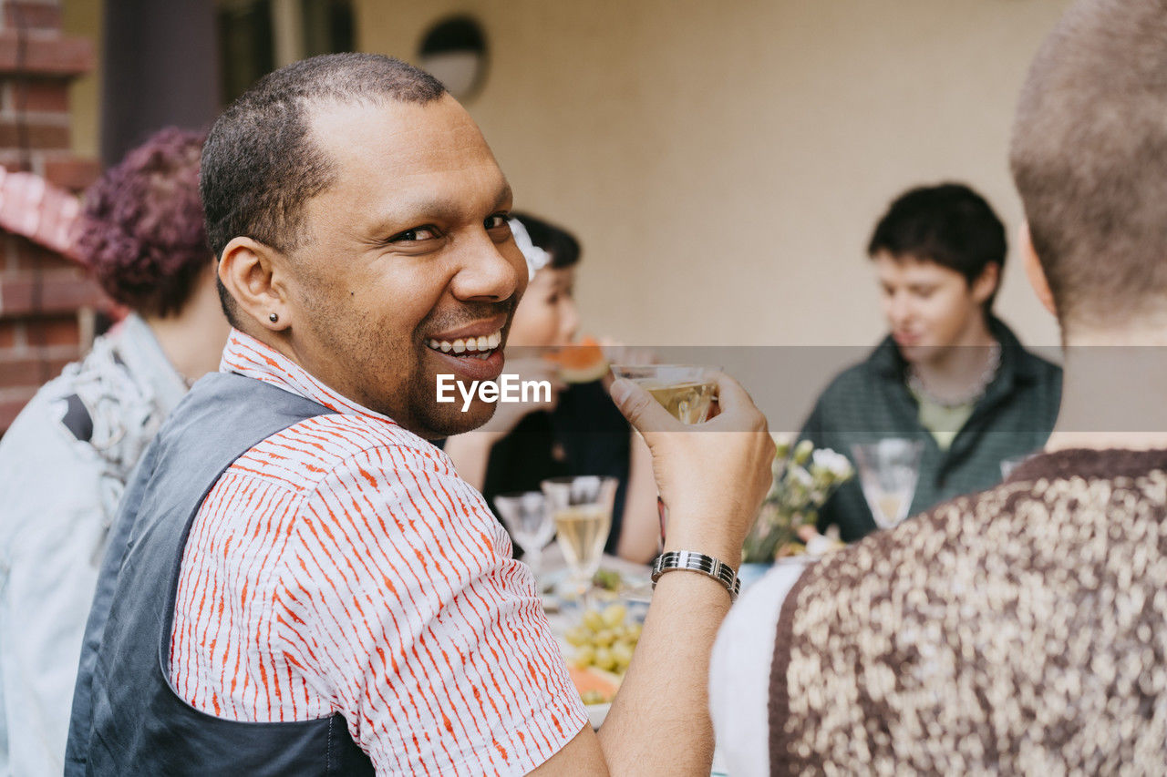Portrait of smiling gay man having drink with friends during party in back yard