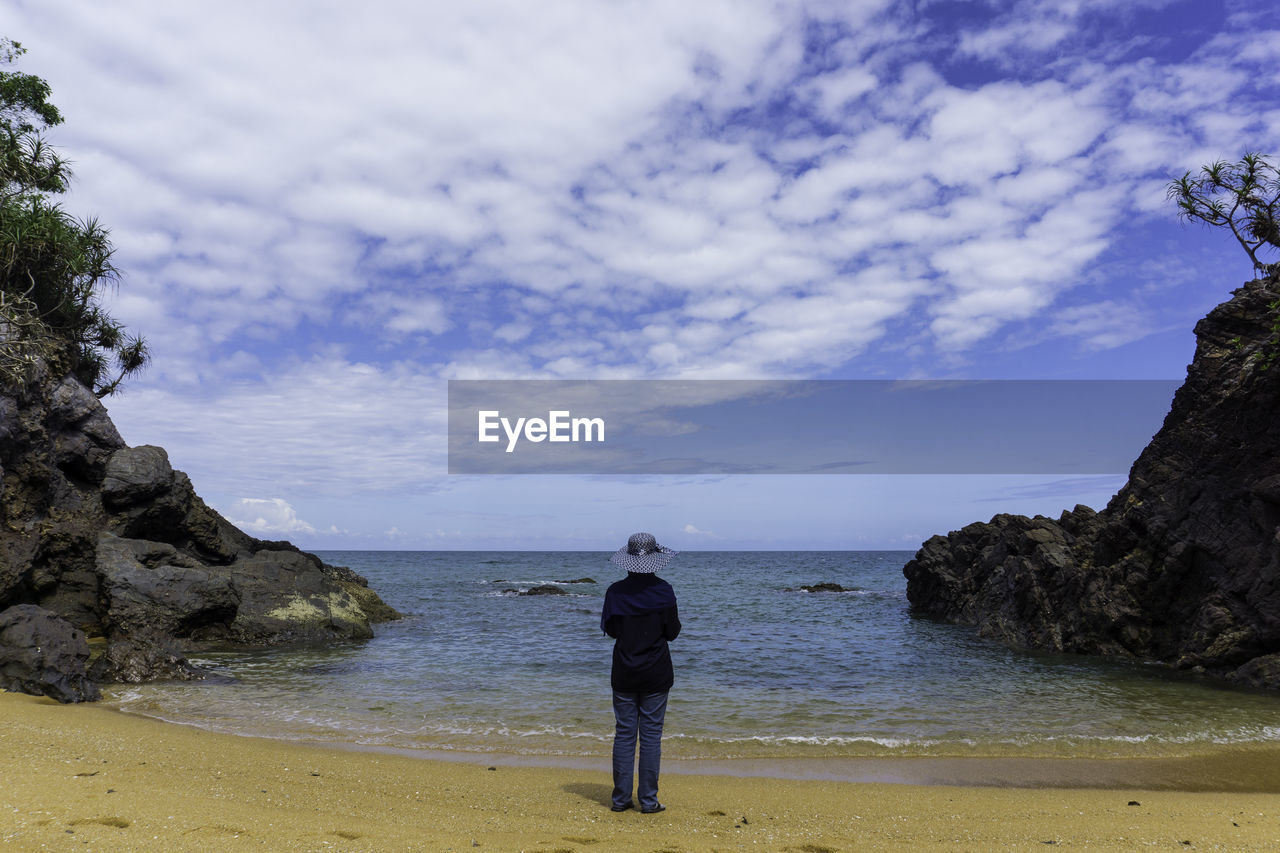 Rear view of man standing on rock at beach against sky