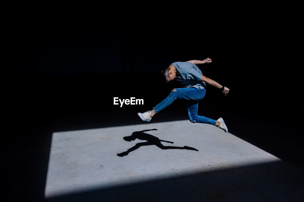 Sunlight falling on young man jumping in darkroom